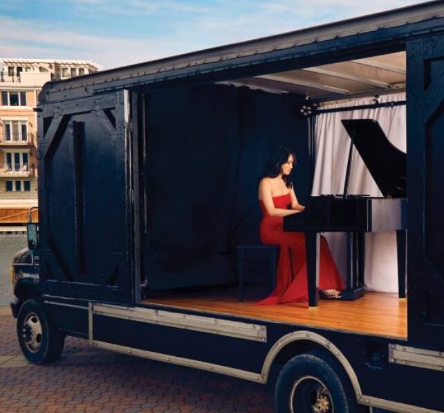 A girl in a red dress plays the piano on a mobile stage.