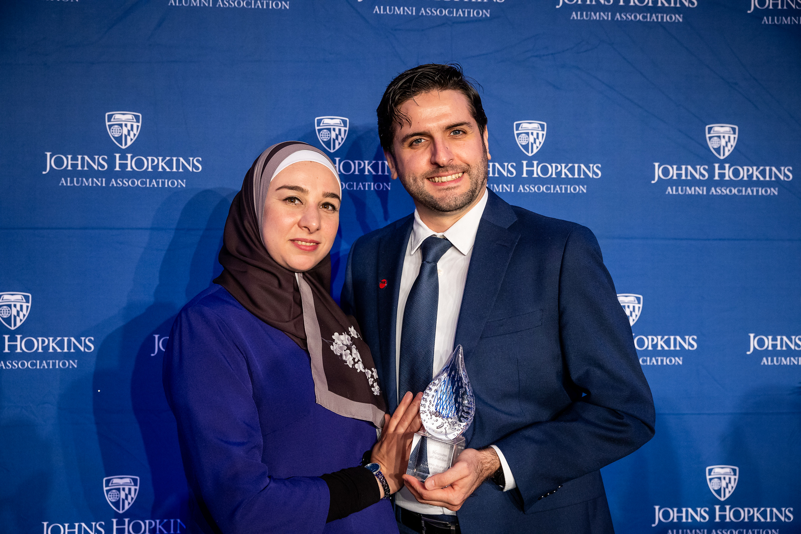 two people standing, one holding a glass award